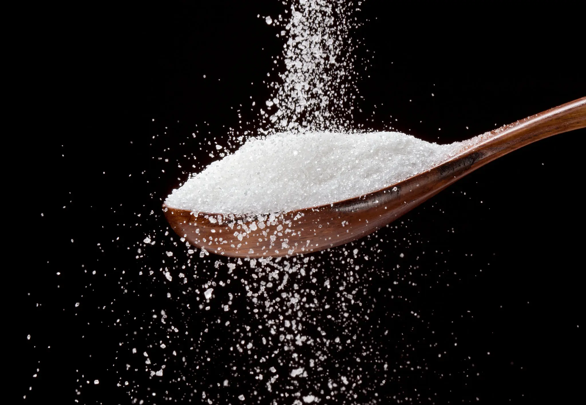 image of granulated sugar pouring onto a wooden spoon against a black background